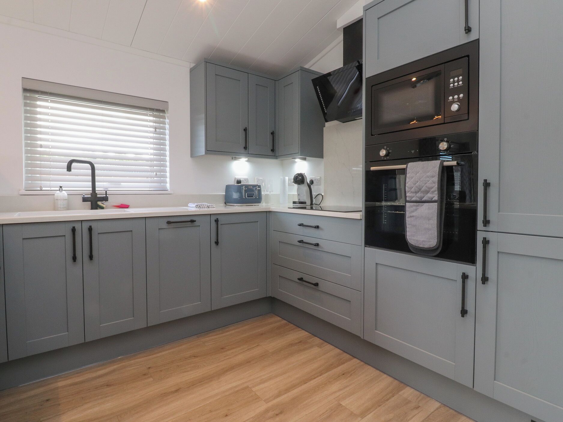 A modern kitchen with grey cabinets, a built-in oven, and a microwave.