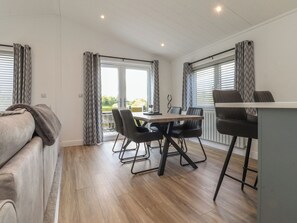 Ein modernes Zimmer mit einer Couch, einem Esstisch mit Stühlen, einer kleinen Küchenzeile und großen Fenstern mit Vorhängen.