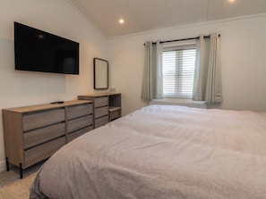Un dormitorio con cama, cómoda, televisor, ventana con cortinas y radiador.