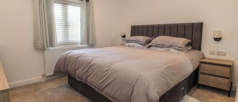 Un dormitorio con cama, mesita de noche, ventana con cortinas y lámpara de pared.