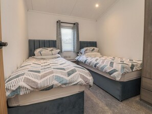 Ein Zweibettzimmer mit zwei Betten, einem Fenster mit Jalousien und einer Deckenleuchte.