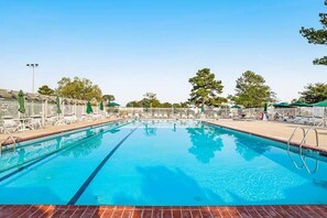 A clear swimming pool with lounge chairs and umbrellas, surrounded by a fence and trees. - Mallard Lakes - 158 Cardinal Ln (Selbyville)