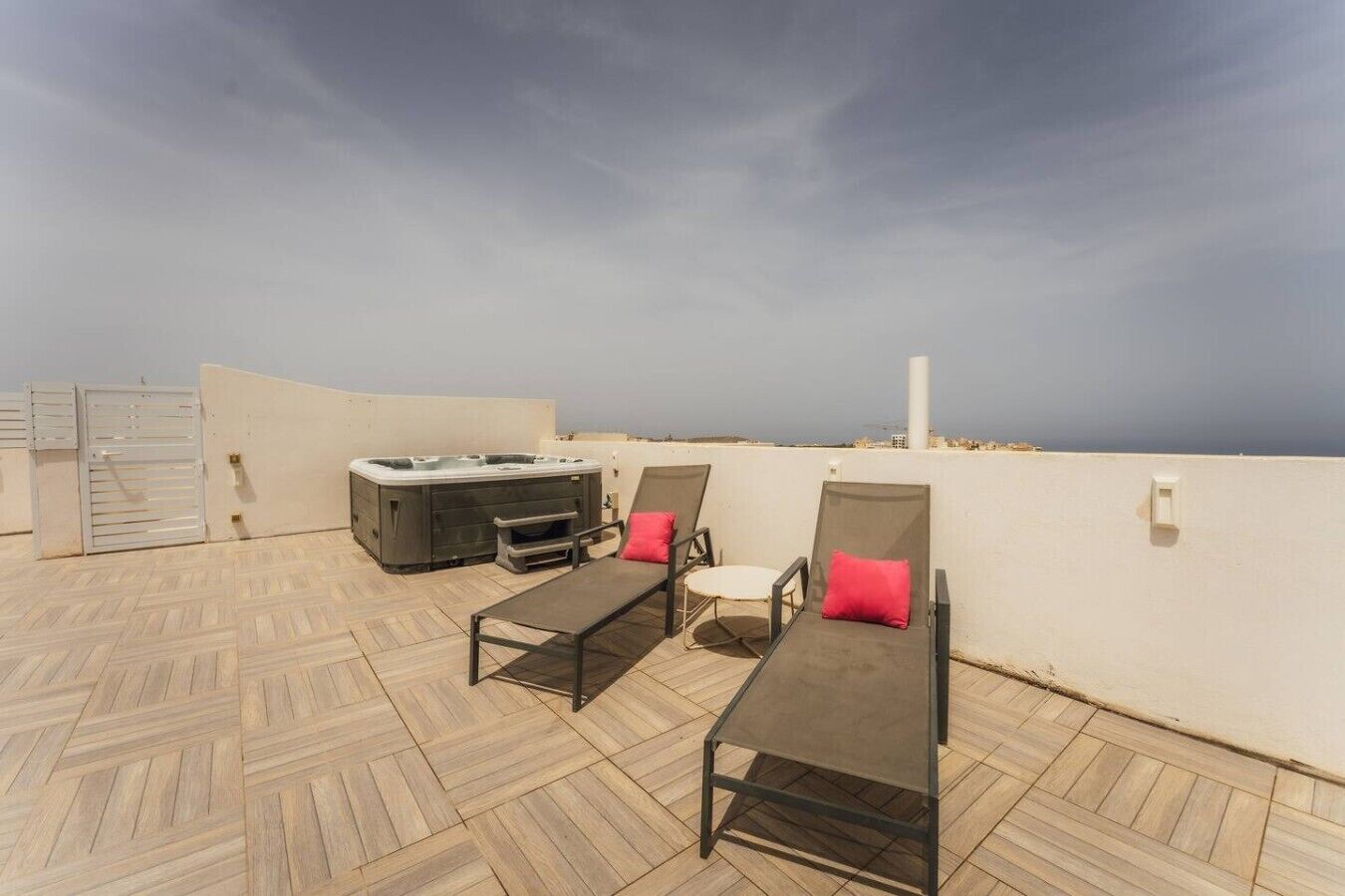 A rooftop terrace with a hot tub, lounge chairs, and a view of the sea.