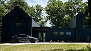 Una casa moderna con un coche estacionado frente a ella, rodeada de árboles.