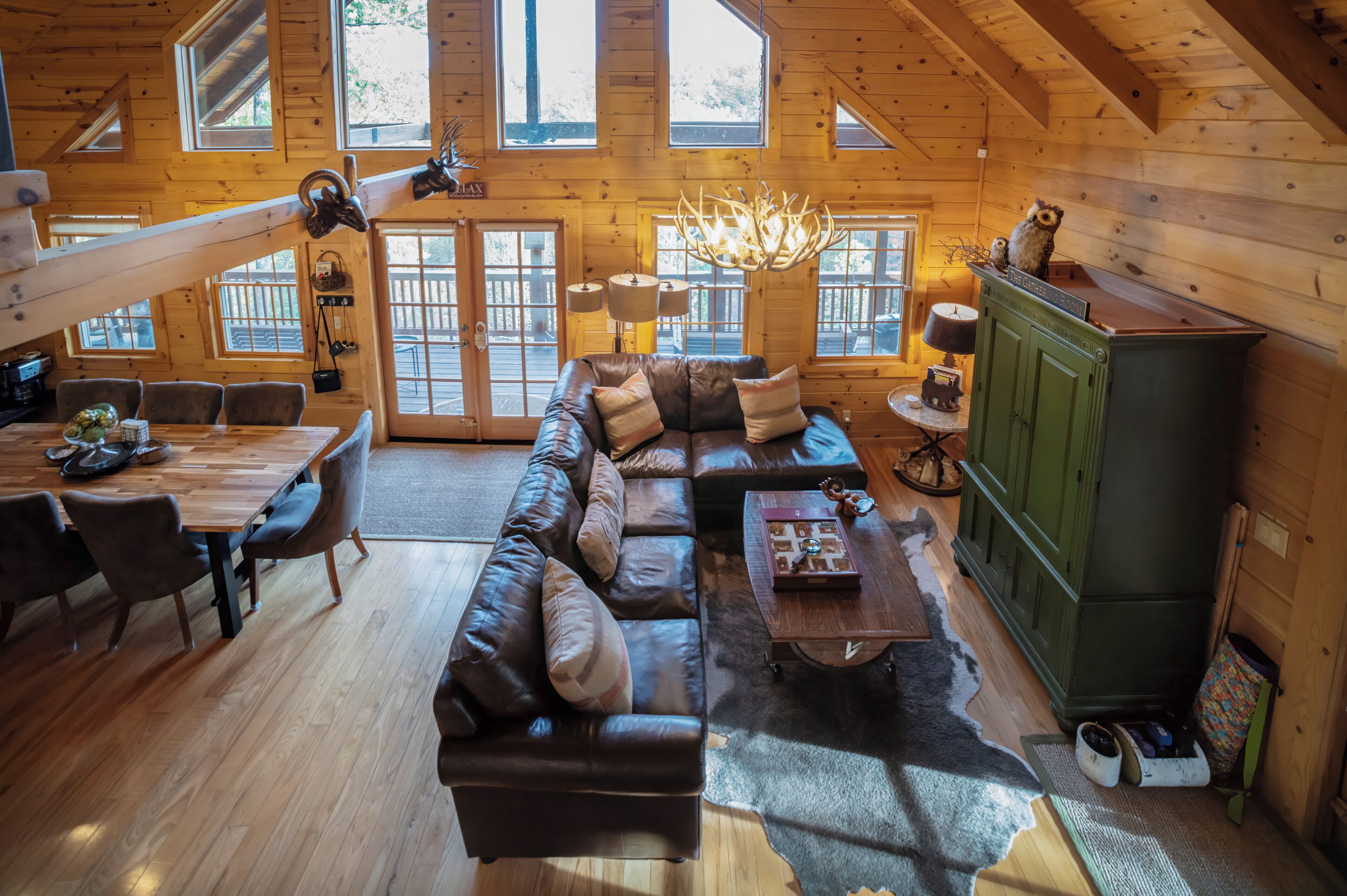 A cozy cabin interior with a leather sofa, dining table, and a green cabinet.