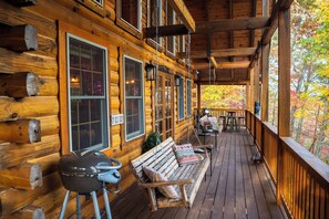 Eine Holzjagdhaus mit Veranda, Grill, Bank und Tisch.