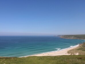 A coastal landscape with a beach, grassy terrain, and a clear blue sky. - Kittiwake (Penzance)