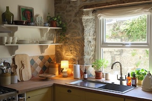 Una cocina con pared de piedra, ventana con vistas y diversos utensilios de cocina.