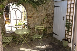 A rustic stone wall, a green metal table and chair, a window with a view, and a white door with a lattice. - Kittiwake (Penzance)
