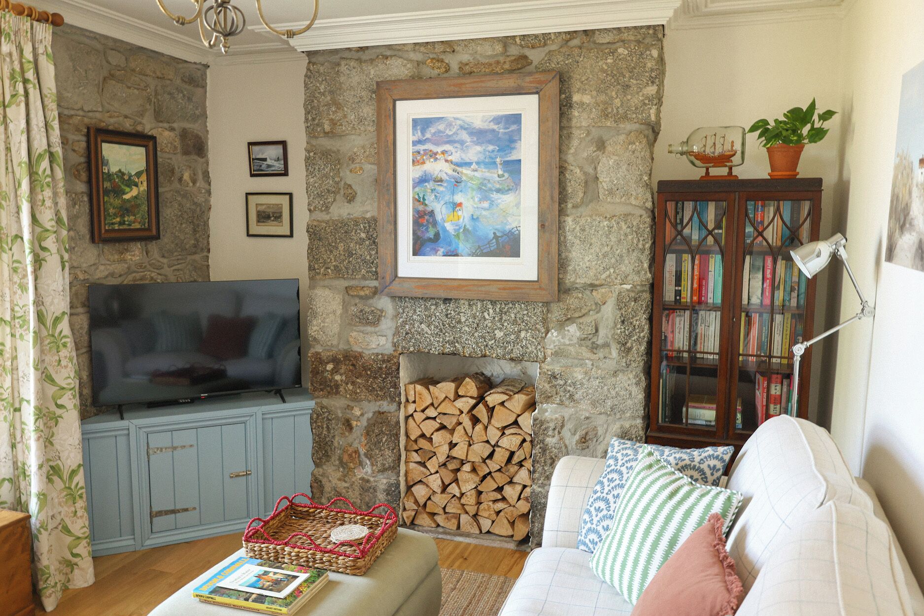 Una sala de estar con pared de piedra, chimenea, televisor, estantería y sofá.