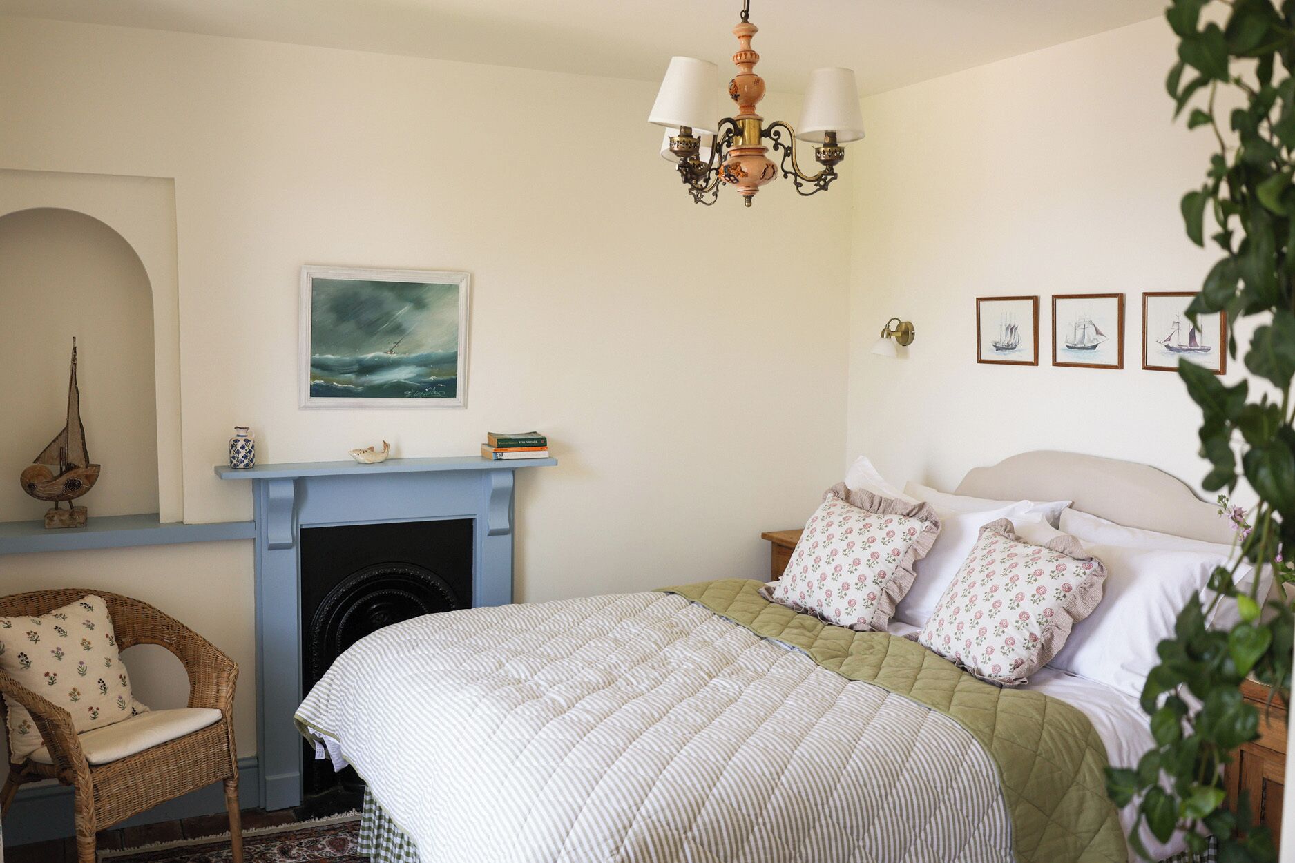 Un dormitorio con cama, chimenea, lámpara colgante, una silla y cuadros en la pared.