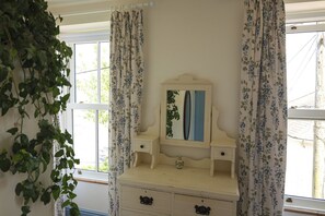 A room with a white dresser, a mirror, and floral curtains. - Kittiwake (Penzance)
