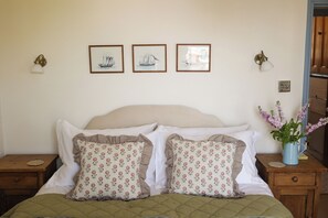 A bedroom with a bed, two nightstands, a vase with flowers, and three framed pictures on the wall. - Kittiwake (Penzance)
