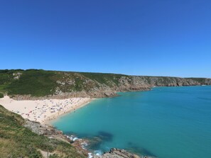 A coastal beach with clear turquoise waters, a sandy shore, and rocky cliffs. - Kittiwake (Penzance)