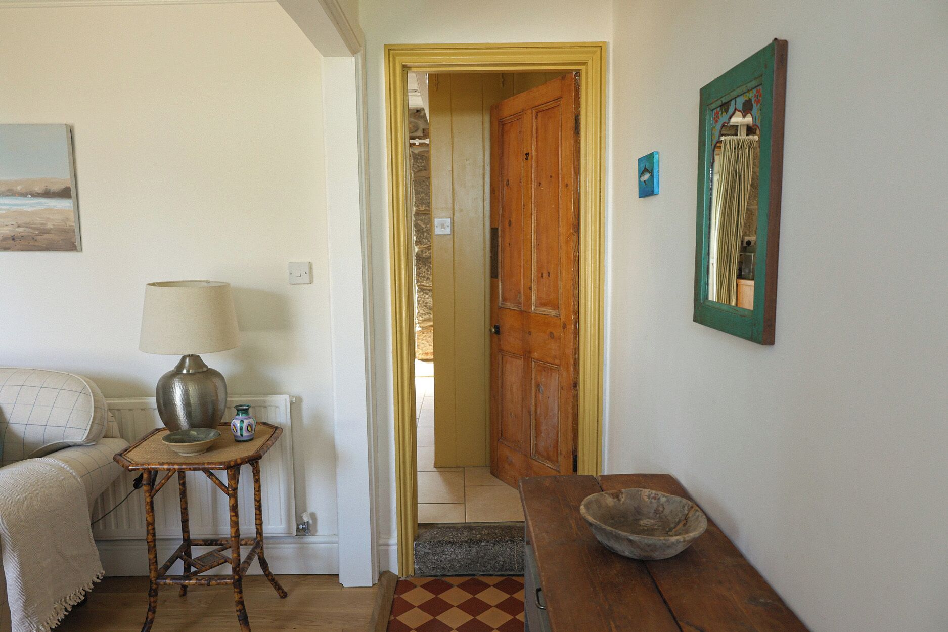 Una habitación con sofá, lámpara, mesa con un cuenco, puerta de madera y espejo adosado a la pared.