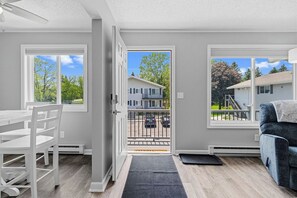 A modern apartment with a dining area, a living room with a sofa, and large windows offering views of a residential neighborhood.