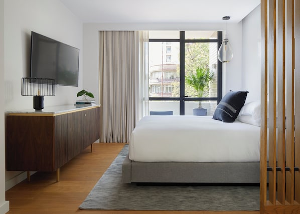 A modern hotel room with a large bed, a TV, a desk, and a view of the city.