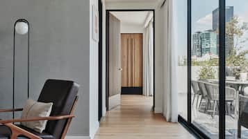 A modern interior with a wooden floor, a black leather chair, a large window with a city view, and a wooden partition in the background.