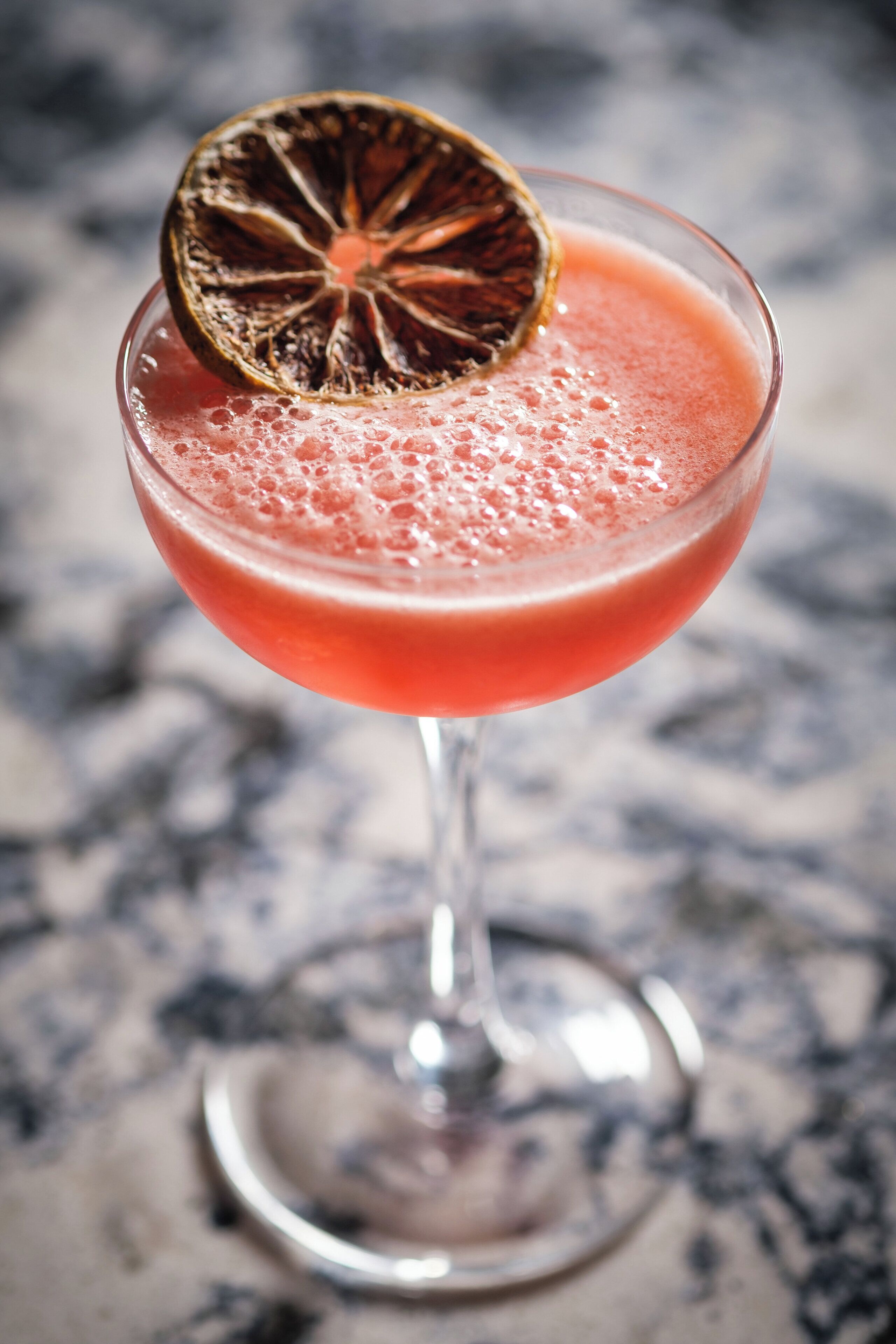 A cocktail in a stemmed glass with a dried fruit garnish on top.