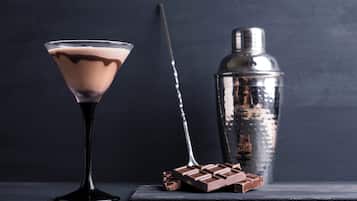 Una copa de martini con una bebida de chocolate, una barra de chocolate y un coctelero sobre una superficie oscura.