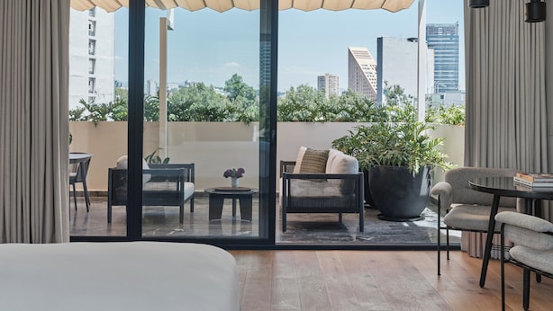 A modern hotel room with a large sliding glass door leading to an outdoor balcony, furnished with a sofa, chairs, and a small table. - Kimpton El Castelar Polanco by IHG (Mexico City)
