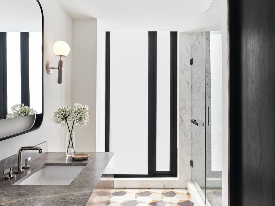 A modern bathroom with a large mirror, two sinks, a shower, and a vase with flowers.