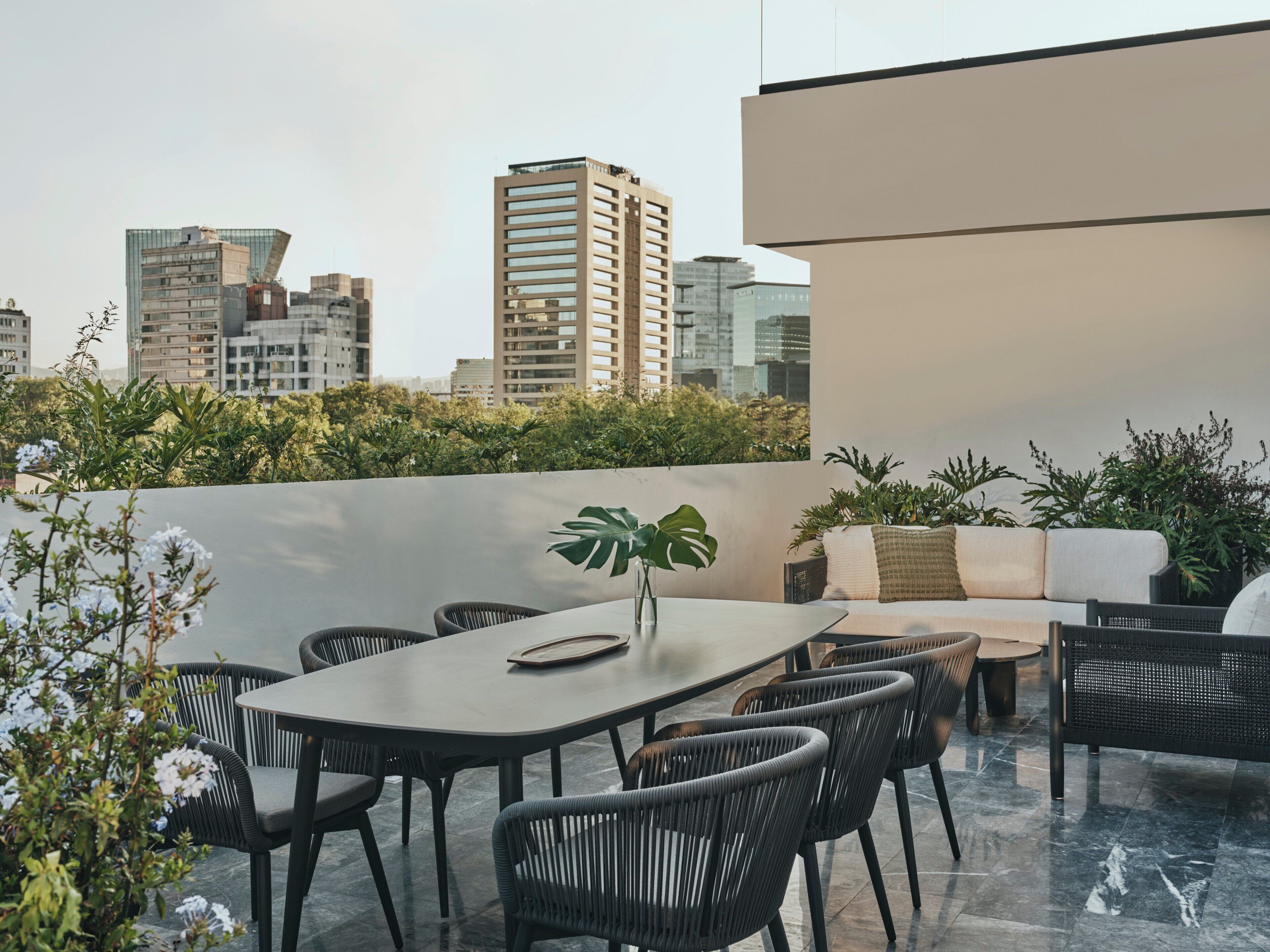 A rooftop terrace with a dining area, seating, and a view of the city skyline.