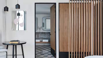 A modern hotel room with a wooden partition, a round table with books, a mirror, and a view into the bathroom.