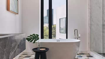 A modern bathroom with a freestanding bathtub, a small side table with a plant, and a geometric tile floor.