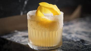 Un vaso con una bebida y una rodaja de fruta sobre una superficie texturizada.