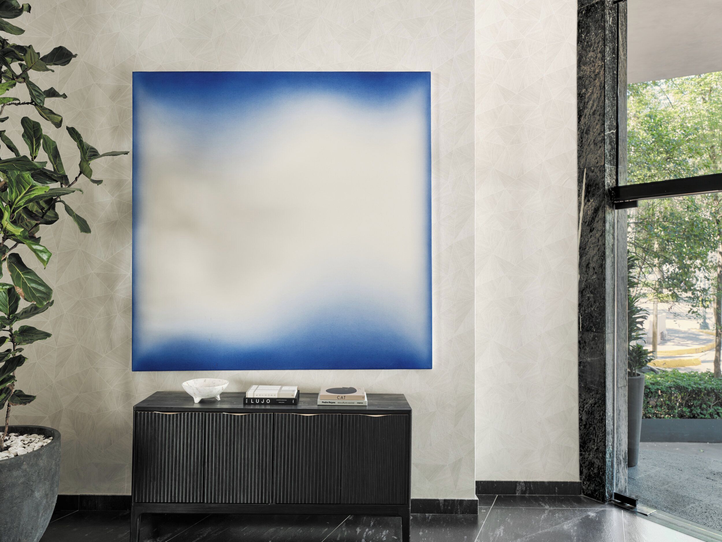 Een modern interieur met een groot abstract schilderij, een zwarte console tafel met boeken en een potplant.
