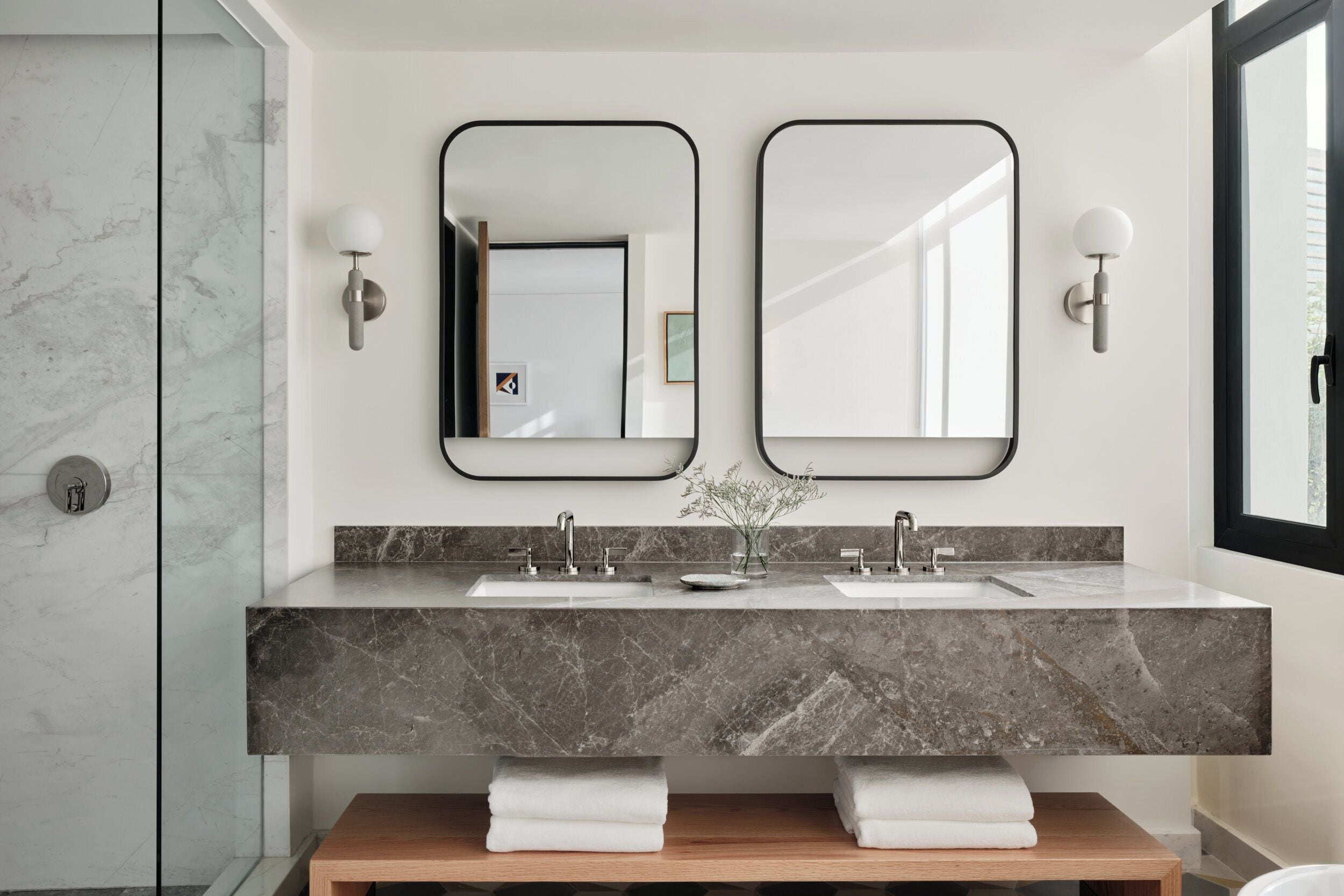 A modern bathroom with two sinks, marble countertops, and wall-mounted mirrors.
