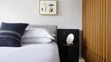Un cuarto de hotel ordenado con cama, almohadas, una mesita de noche con lámpara, una obra de arte enmarcada en la pared y un panel de madera a la derecha.
