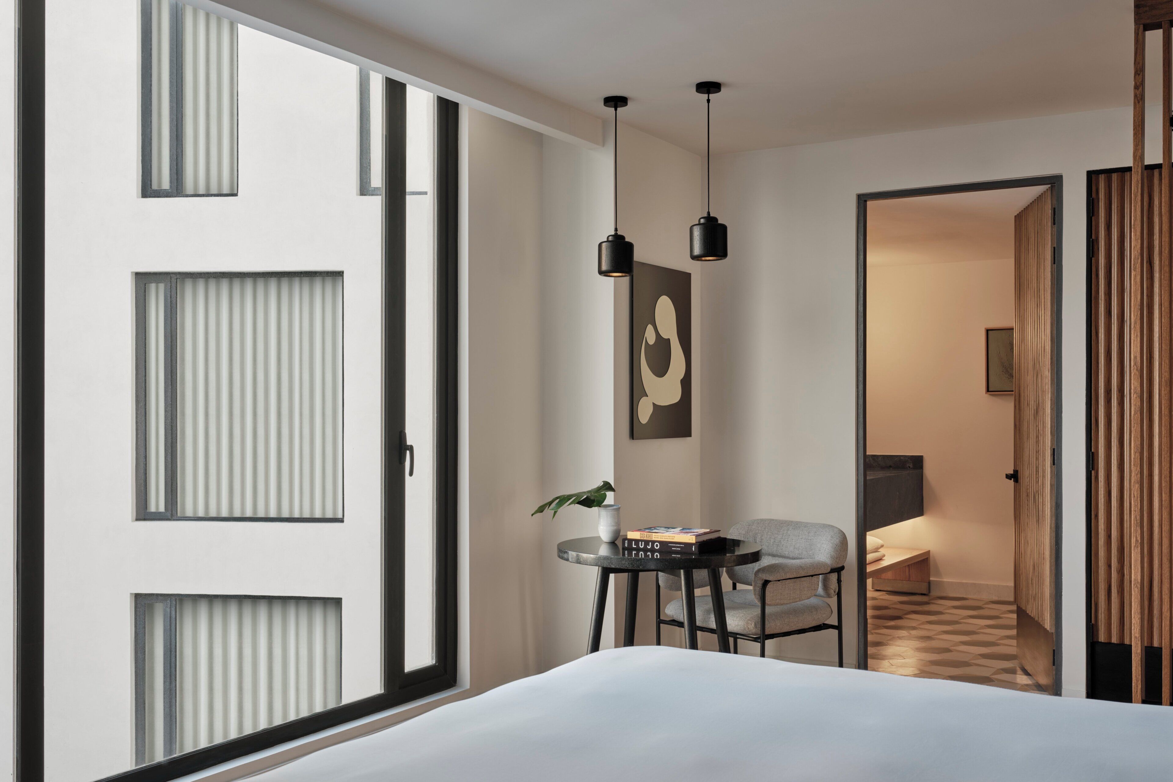 Una habitación de hotel moderna con una cama grande, una mesita con una planta, una silla y una puerta que da al baño.