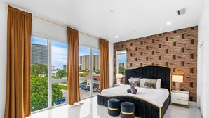 Ein modernes Schlafzimmer mit einem großen Bett, Blick auf die Stadt und einer Wand mit Ziegelsteinmuster.