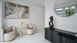 Una sala moderna con un cuadro abstracto grande, dos sillones redondos, una pequeña mesa con una escultura, un mueble bajo oscuro y un espejo redondo que refleja una vista al exterior.