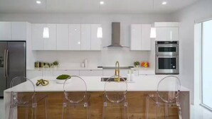 Una cocina moderna con armarios blancos, electrodomésticos de acero inoxidable y una isla de madera con taburetes de bar.