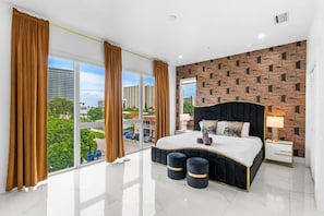 Ein modernes Schlafzimmer mit einem großen Bett, Blick auf die Stadt und einer Wand mit Ziegelsteinmuster.
