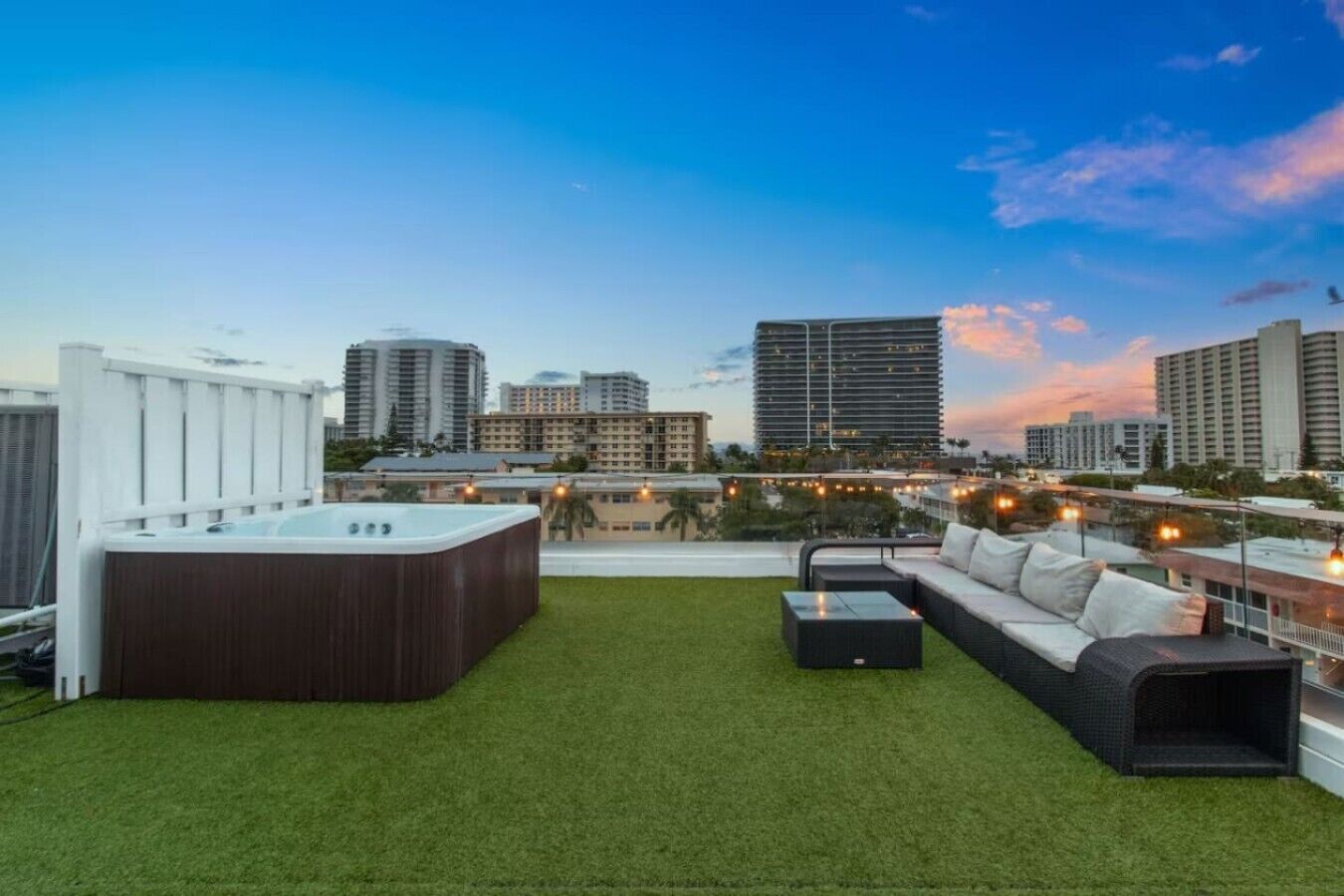 Une terrasse sur le toit avec un jacuzzi, des sièges extérieurs et une vue sur la ville au crépuscule.