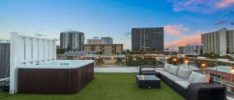 Une terrasse sur le toit avec un jacuzzi, des sièges extérieurs et une vue sur la ville au crépuscule.