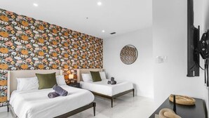 Habitación de hotel con dos camas, un papel tapiz con estampado floral, un adorno redondo en la pared y un televisor de pantalla plana montado.