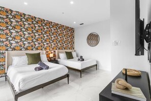 Ein Hotelzimmer mit zwei Betten, einer großen Wand mit floralem Muster, einem runden Wanddekor und einem an der Wand befestigten Flachbildfernseher.