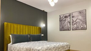A bed with a green upholstered headboard, a patterned bedspread, and two wall-mounted artworks depicting foliage. - Luxurious apartment 5 min from Mohamed 5 airport (Casablanca)