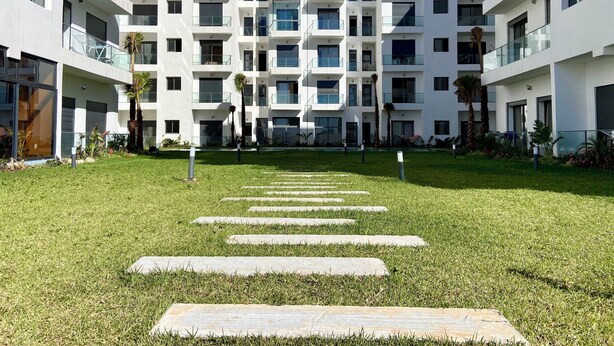 A modern multi-story building with balconies, a central courtyard with stone steps, and surrounding greenery. - Luxurious apartment 5 min from Mohamed 5 airport (Casablanca)