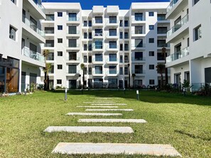 Un edifici modern d'alguns pisos amb balcons, un pati central amb escales de pedra i vegetació al voltant.