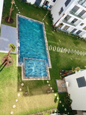 Ein Pool auf dem Dach mit klarem, blauem Wasser, umgeben von gepflegten Rasenflächen und Palmen.
