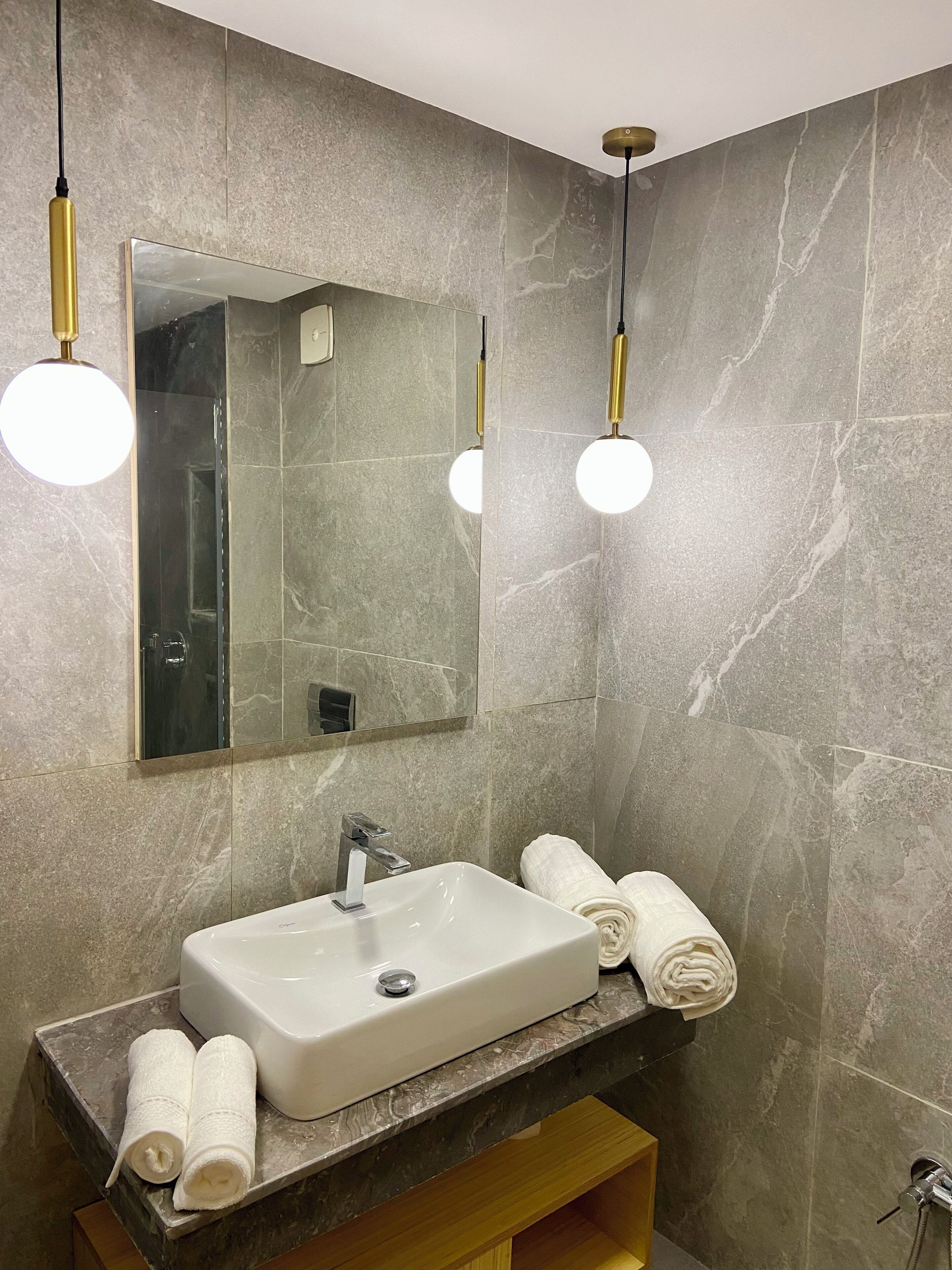 A modern bathroom with a large mirror, a white sink, and two round light fixtures.