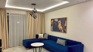 A modern living room with a blue sofa, a round table, and a ceiling light fixture. - Luxurious apartment 5 min from Mohamed 5 airport (Casablanca)