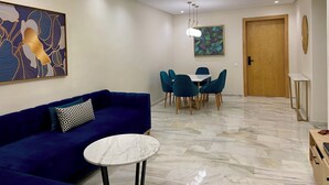 A modern living room with a blue sofa, a round coffee table, and a dining area with teal chairs. - Luxurious apartment 5 min from Mohamed 5 airport (Casablanca)