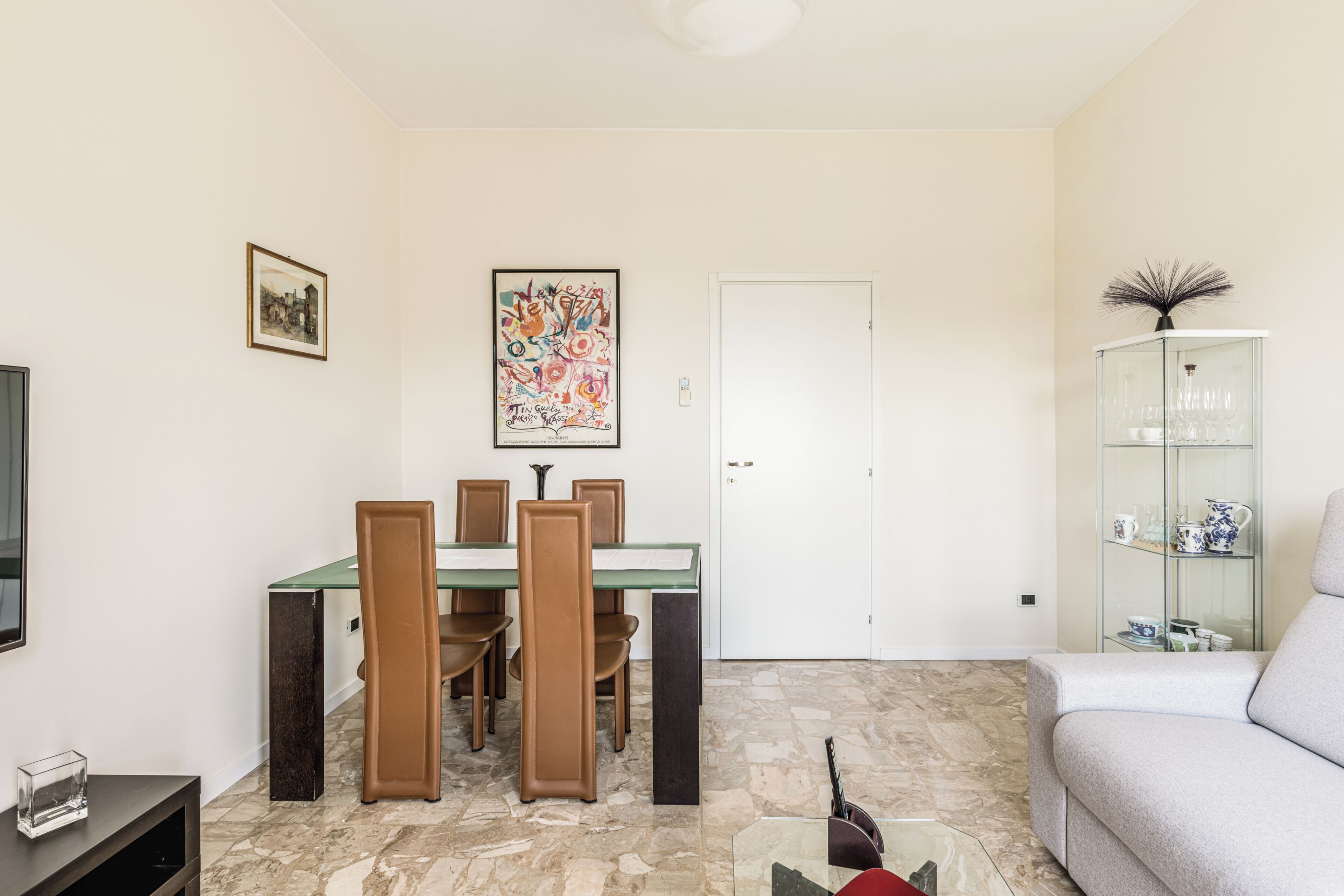 A dining area with a table and chairs, a glass cabinet with decorative items, and a television on a stand.